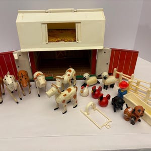 Puede incluir: Un juego de granja de juguete vintage con un granero blanco con puertas rojas y varios animales de granja de plástico. El juego incluye vacas, caballos, ovejas, gallinas, un perro, una figura de granjero y una valla. El granero mide unos 30 cm de ancho.