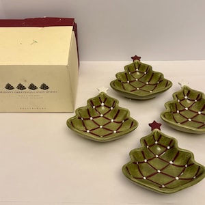 Può includere: Set di quattro piattini di caramelle a forma di albero di Natale in ceramica verde con dettagli rossi e bianchi. Ogni piatto ha una stella in cima. La scatola recita "Season's Greetings Candy Dishes".