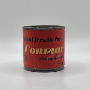 May include: A cylindrical red can with black trim and the text "Listen! it calls for... Conmar the major tip" in yellow and white. The can has a slightly distressed appearance, suggesting it is vintage.
