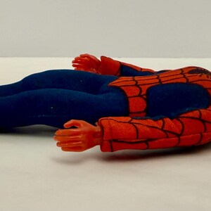 Puede incluir: Una mu&ntilde;eca vintage de Spider-Man en posici&oacute;n horizontal. La mu&ntilde;eca lleva un traje rojo y negro con telara&ntilde;as y pantalones azules. La cabeza de la mu&ntilde;eca es roja con detalles de ojos blancos, y sus manos y pies son rojos.