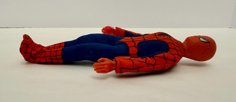 Puede incluir: Una mu&ntilde;eca vintage de Spider-Man en posici&oacute;n horizontal. La mu&ntilde;eca lleva un traje rojo y negro con telara&ntilde;as y pantalones azules. La cabeza de la mu&ntilde;eca es roja con detalles de ojos blancos, y sus manos y pies son rojos.