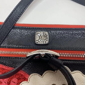 May include: Black leather crossbody bag with red accents and a silver-tone buckle. The bag features a decorative silver square clasp and a black strap. The Brighton brand name is visible on the buckle.