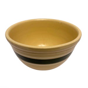 Puede incluir: Un cuenco mezclador de cerámica amarilla con un diseño de rayas blancas y negras. El cuenco tiene forma redondeada y un acabado liso y brillante. El cuenco es adecuado para mezclar ingredientes o servir alimentos.