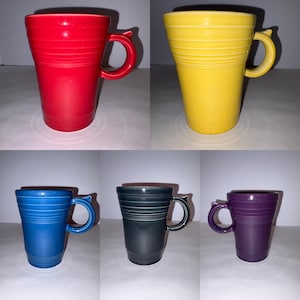 May include: A collection of five ceramic mugs in red, yellow, blue, black, and purple. Each mug features a tapered cylindrical body with horizontal ribbed detailing near the rim and a curved handle extending from the side of the vessel.
