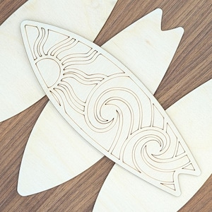 May include: A light-colored wooden surfboard cutout featuring a laser-cut design of a sun and ocean waves. The surfboard shape has a pointed nose and a swallow tail, with the intricate sun and wave patterns carved out of the center surface.