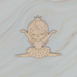 May include: A wooden cutout of a ballerina in a split, wearing a crown and tutu. The ballerina has her arms outstretched and is smiling. The cutout is made of light-colored wood and is suitable for crafts.
