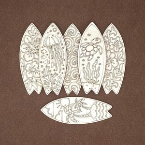 May include: Six light-colored wooden surfboard cutouts featuring engraved designs. Five are arranged vertically with patterns of hibiscus flowers, a jellyfish, swirls, a sea turtle, and more flowers. One surfboard lies horizontally with palm trees.