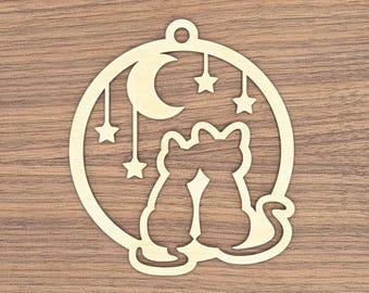 May include: A wooden ornament featuring two cats silhouetted against a crescent moon and stars. The cats are inside a circular frame with a small hole at the top for hanging. The ornament is made of light-colored wood.