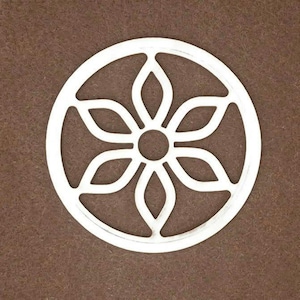 May include: A circular white cutout featuring a symmetrical six-petaled flower design enclosed within a thin outer ring. The central portion of the flower consists of a small solid circle, with six petal shapes radiating outward to the frame.