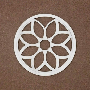 May include: A white circular cutout featuring a symmetrical floral pattern with eight petal-like shapes radiating from a central octagonal opening, enclosed within a thin outer ring border, creating a geometric design.