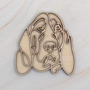 May include: A wooden cutout of a dog's head in a line art style. The dog's eyes, nose, and mouth are detailed, and the ears are floppy.