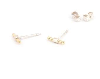 Könnte beinhalten: Ein Paar kleine Ohrstecker mit T-Bar-Design. Die Ohrringe haben einen silberfarbenen Stift und einen goldfarbenen Balken. Zwei Ohrringverschlüsse sind ebenfalls sichtbar. Auf weißem Hintergrund.