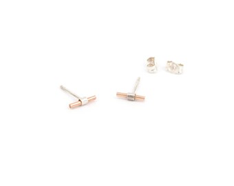 May include: A pair of silver and rose gold bar stud earrings with matching earring backs. The earrings have a T-bar design with a silver center and rose gold ends. The earrings are displayed on a white background.