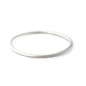 May include: A simple, silver-colored bangle bracelet. The round bracelet is made of a solid metal and has a smooth, matte finish. The bangle is shown on a white background.