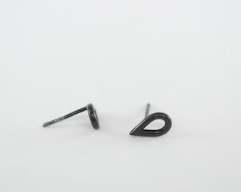 Könnte beinhalten: Ein Paar kleine, schwarze Ohrstecker in Tropfenform. Die Ohrringe haben ein schlichtes, minimalistisches Design mit einem Stift zum Einsetzen. Die Ohrringe sind vor einem weißen Hintergrund platziert.
