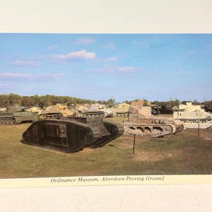 May include: Vintage postcard featuring a collection of military tanks on display at the Ordnance Museum, Aberdeen Proving Ground. The tanks are various colors, including green, brown, and tan, set against a blue sky.