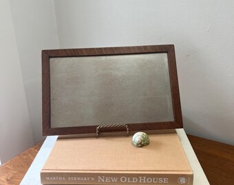 May include: A rectangular wooden picture frame with a light-colored interior rests on two books. The top book is titled "New Old House" by Martha Stewart. A small seashell sits on top of the book.