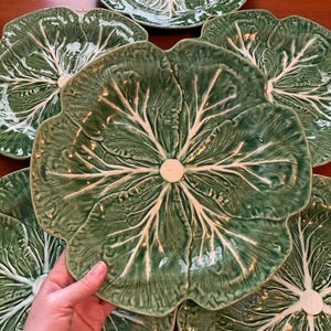 May include: A set of five ceramic plates shaped like green cabbage leaves. Each plate features a textured surface with raised white veins radiating from a central point, mimicking the appearance of a natural leaf with scalloped edges.