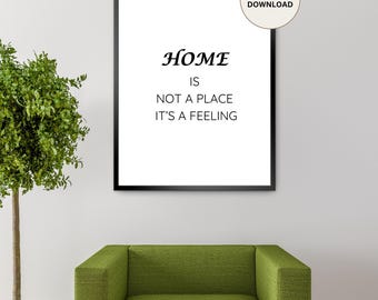 May include: A framed print with the words "HOME IS NOT A PLACE IT'S A FEELING" in black font. The print is in a black frame and is labeled "DIGITAL DOWNLOAD". A green armchair and a small tree are in the foreground.