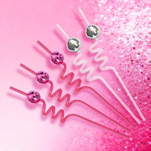 May include: A collection of decorative cocktail straws. The straws are pink and white, with a spiral design. Each straw is topped with a small disco ball. The background is a glittery pink.