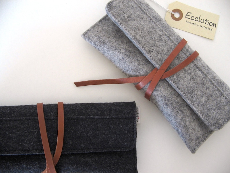 Two deluxe glasses cases in black and silver gray soft merino wool felt, adorned with a distinctive leather wrap-around closure