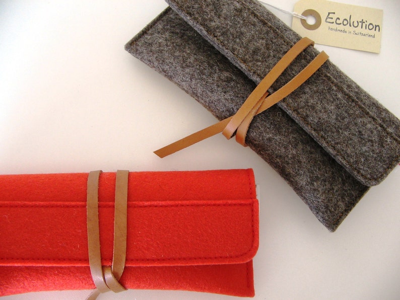 Two deluxe glasses cases in mango red and natural gray soft merino wool felt, adorned with a distinctive leather wrap-around closure