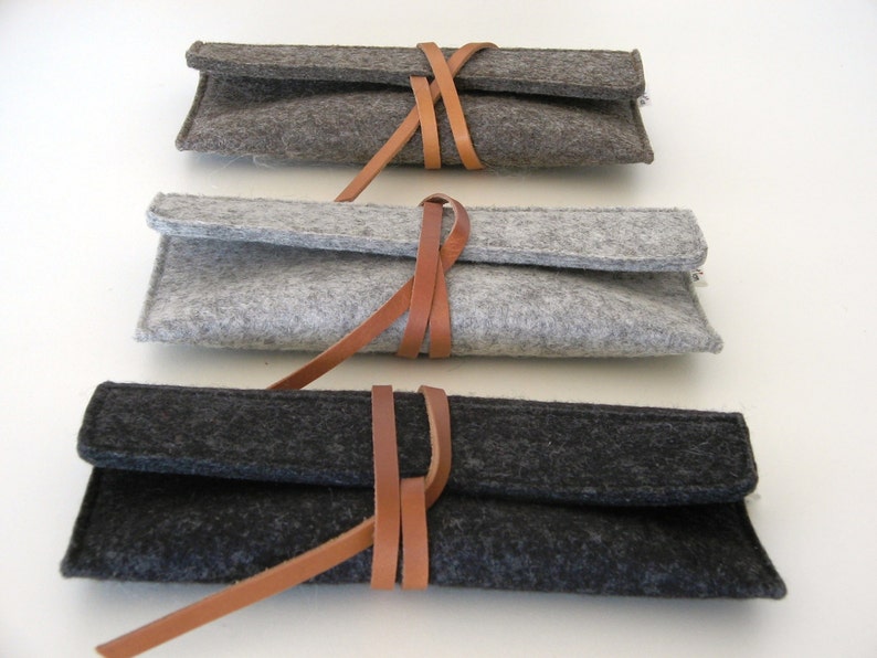 Three soft wool felt reading glass cases in black silver and natural gray featuring a unique leather wrap around closure