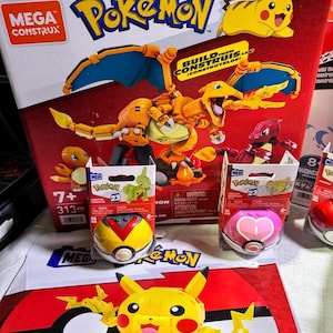 Puede incluir: Una colecci&oacute;n de sets de construcci&oacute;n Mega Construx con tem&aacute;tica Pok&eacute;mon. La imagen presenta una caja grande con un modelo de Charizard, cajas m&aacute;s peque&ntilde;as con figuras de Pok&eacute;mon y varios contenedores con forma de Pok&eacute; Ball. La combinaci&oacute;n de colores es principalmente roja, amarilla y naranja.