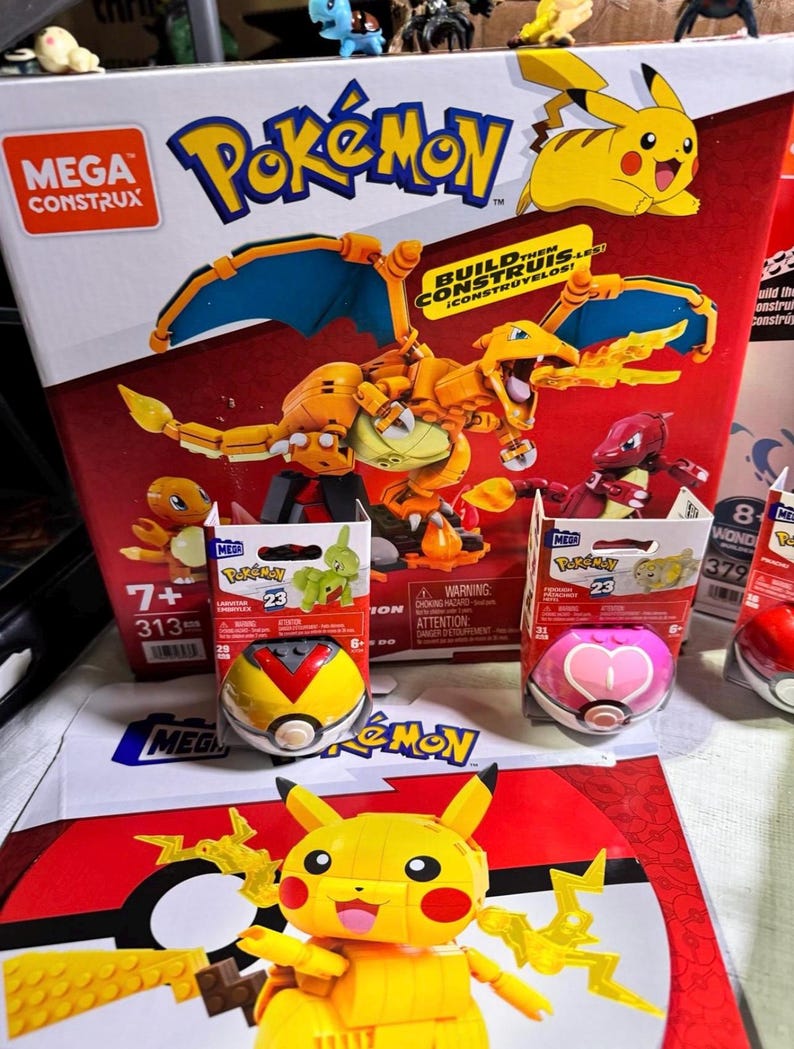 Puede incluir: Una colecci&oacute;n de sets de construcci&oacute;n Mega Construx con tem&aacute;tica Pok&eacute;mon. La imagen presenta una caja grande con un modelo de Charizard, cajas m&aacute;s peque&ntilde;as con figuras de Pok&eacute;mon y varios contenedores con forma de Pok&eacute; Ball. La combinaci&oacute;n de colores es principalmente roja, amarilla y naranja.