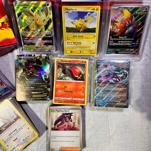 Puede incluir: Una colecci&oacute;n de cartas coleccionables de Pok&eacute;mon calificadas, incluyendo Pikachu, Leafeon y Sizzlipede. Las cartas est&aacute;n en protectores, con etiquetas de calificaci&oacute;n visibles. Las cartas se muestran sobre una superficie clara.