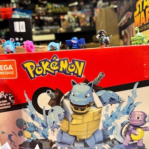Puede incluir: Una caja roja de Mega Construx Pok&eacute;mon con una gran figura de Blastoise y figuras de Pok&eacute;mon m&aacute;s peque&ntilde;as. La caja tiene el logotipo de Pok&eacute;mon y varios personajes. Varias figuras peque&ntilde;as de Pok&eacute;mon est&aacute;n encima de la caja.