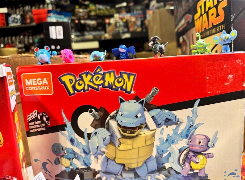 Puede incluir: Una caja roja de Mega Construx Pok&eacute;mon con una gran figura de Blastoise y figuras de Pok&eacute;mon m&aacute;s peque&ntilde;as. La caja tiene el logotipo de Pok&eacute;mon y varios personajes. Varias figuras peque&ntilde;as de Pok&eacute;mon est&aacute;n encima de la caja.