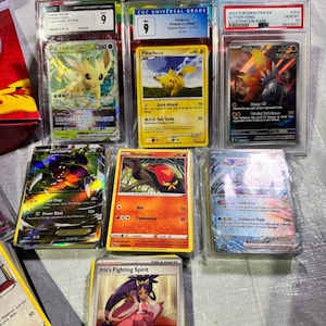 Puede incluir: Una colecci&oacute;n de cartas coleccionables de Pok&eacute;mon calificadas, incluyendo cartas de Pikachu y Leafeon VSTAR, en protectores. Las cartas presentan varios personajes y dise&ntilde;os, con calificaciones y texto visibles.