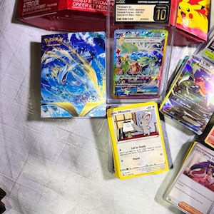 Puede incluir: Una colecci&oacute;n de cartas coleccionables de Pok&eacute;mon, incluyendo cartas clasificadas en estuches protectores. La imagen presenta varios dise&ntilde;os de cartas, incluyendo una con el texto "Minccino" y otra con "Iris's Fighting Spirit".