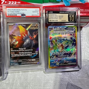 Puede incluir: Dos cartas coleccionables de Pok&eacute;mon clasificadas en estuches protectores. Una carta presenta una ilustraci&oacute;n de Slither Wing, la otra una carta de Terapagos ex. Ambas cartas est&aacute;n clasificadas como Gem Mint 10 por CGC.