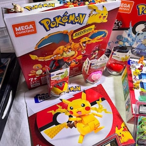Puede incluir: Una colecci&oacute;n de sets de construcci&oacute;n y figuras de Pok&eacute;mon de Mega Construx. Las cajas son rojas y blancas, con Pikachu y otros personajes. Una figura de Pikachu est&aacute; montada sobre una base roja y blanca con el tema de la Pok&eacute; Ball. Se muestran varias figuras de Pok&eacute;mon.