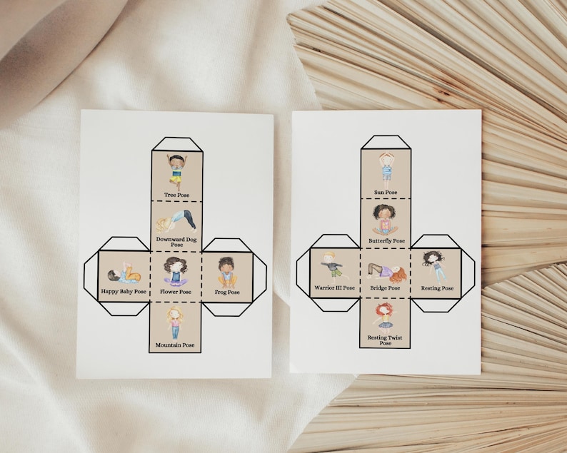 Pode incluir: Dois cart&otilde;es brancos com ilustra&ccedil;&otilde;es de posturas de ioga. Cada cart&atilde;o apresenta um design de cubo com desenhos de crian&ccedil;as demonstrando posturas como Postura da &Aacute;rvore, Postura do C&atilde;o Virado para Baixo e Postura do Beb&ecirc; Feliz. Os cart&otilde;es est&atilde;o em uma superf&iacute;cie bege.