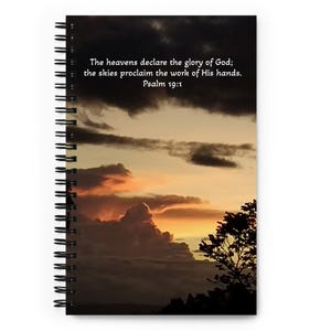 Könnte beinhalten: Spiralgebundenes Notizbuch mit einem Sonnenuntergangsbild, dunklen Wolken und einer Baumsilhouette. Auf dem Cover steht der Text "The heavens declare the glory of God; the skies proclaim the work of His hands. Psalm 19:1".