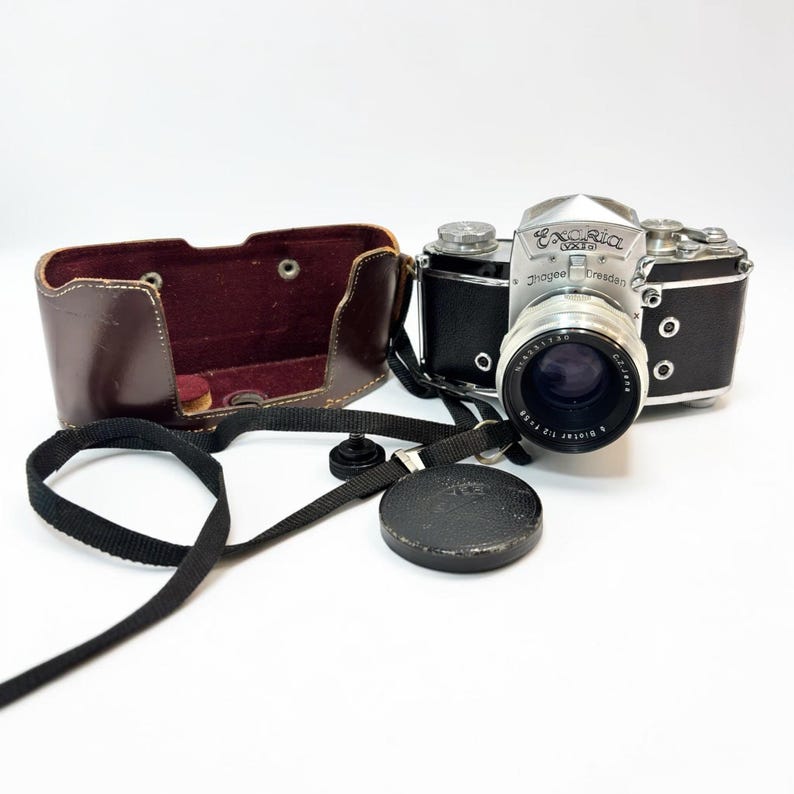 Puede incluir: Una c&aacute;mara vintage Exakta Varex con cuerpo negro y placa superior plateada, que presenta el texto Ihagee Dresden. Incluye un objetivo con el texto Biotar 1:2 f=58, una tapa de objetivo negra, una correa negra y un estuche de cuero marr&oacute;n.