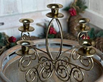 May include: Gold metal candelabra with five candle holders. The candelabra has a decorative, swirling design and is sitting on a wooden tray.