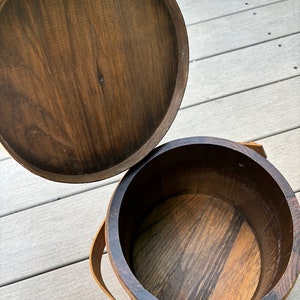May include: A wooden bucket with a lid, the lid is open and the bucket is empty. The bucket has a brown wooden handle.