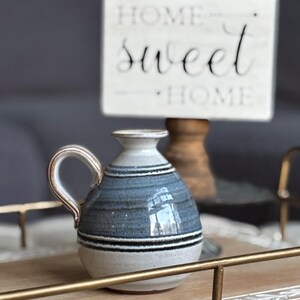May include: A small, blue and white ceramic pitcher with a handle. The pitcher has a striped design and is sitting on a wooden surface.