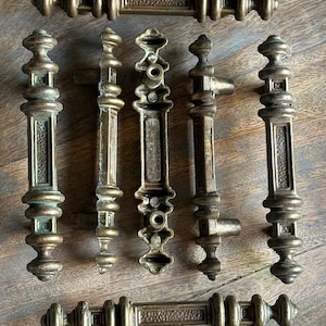 May include: Set of eight antique brass cabinet door pulls with ornate designs. The pulls have a textured finish and are in excellent condition.