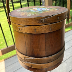 May include: A wooden bucket with a painted floral design on the lid. The bucket has a handle and is made of natural wood.