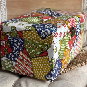 May include: A rectangular patchwork fabric box with a brass handle and clasp. The box is covered in a quilt-like pattern of various floral and geometric prints in red, green, blue, and yellow. The box is approximately 12 inches long, 8 inches wide, and 6 inches high.