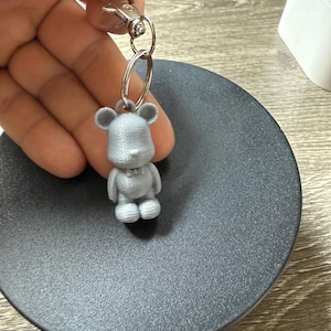 May include: A silver-colored bear keychain with a silver ring and a silver clip.