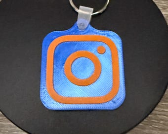 May include: A blue and orange Instagram logo keychain. The logo is a square with rounded corners and features a white camera icon inside.