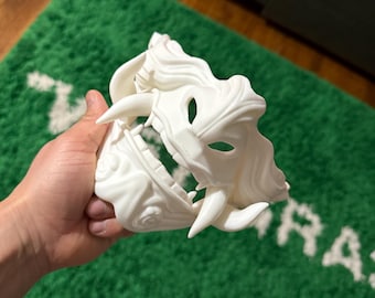 May include: White plastic mask with a detailed design of a snarling animal face. The mask has sharp teeth and a textured surface.