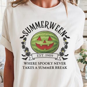 May include: Cream-colored t-shirt featuring a watermelon-carved jack-o'-lantern design with the text "SUMMERWEEN EST. 1989 WHERE SPOOKY NEVER TAKES A SUMMER BREAK". The design includes bats and floral accents, perfect for Halloween.