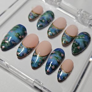 May include: A set of ten false nails with a water lily design. The nails are oval shaped and have a light pink base with a gold accent. The water lily design is painted in shades of blue, green, and pink.